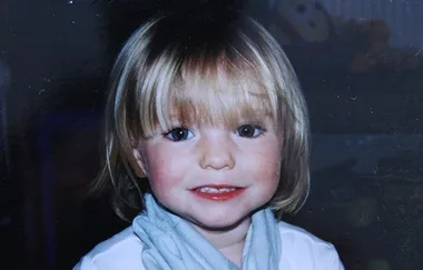 A smiling young child with blonde hair and blue eyes, wearing a light blue scarf over a white top.