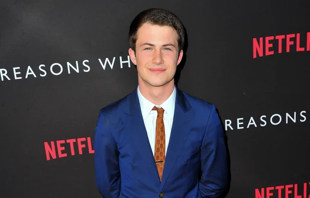 Young man in a blue suit stands on a red carpet in front of a Netflix promotional backdrop.
