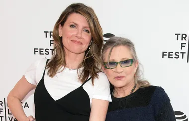 Two people smiling at the Tribeca Festival, one in a white top and black dress, the other in glasses and a dark sweater.
