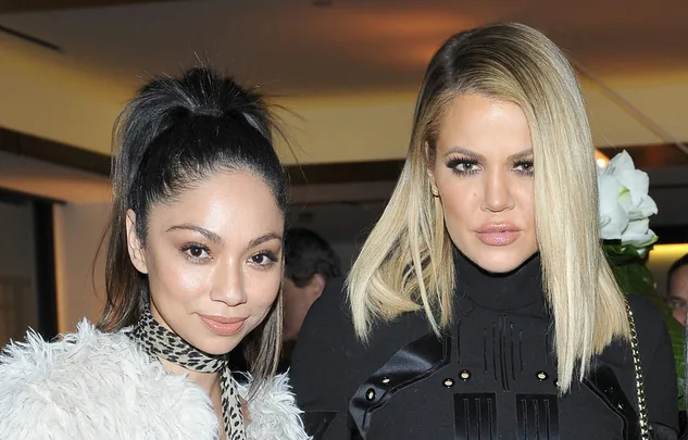 Two women posing at an event, one with a high ponytail and faux fur coat, the other with blonde hair and a black outfit.
