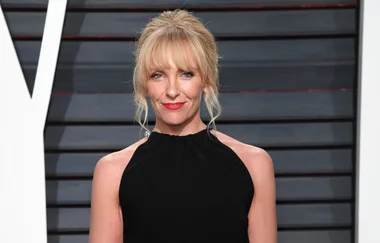 Woman with blonde hair in a black halter dress, posing indoors against a striped background.