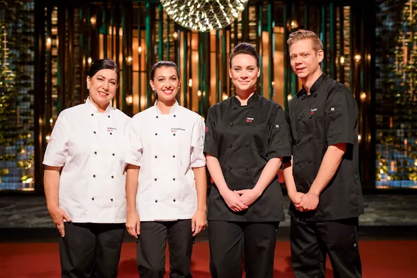 Four chefs in white and black uniforms pose together in a lit dining setting.