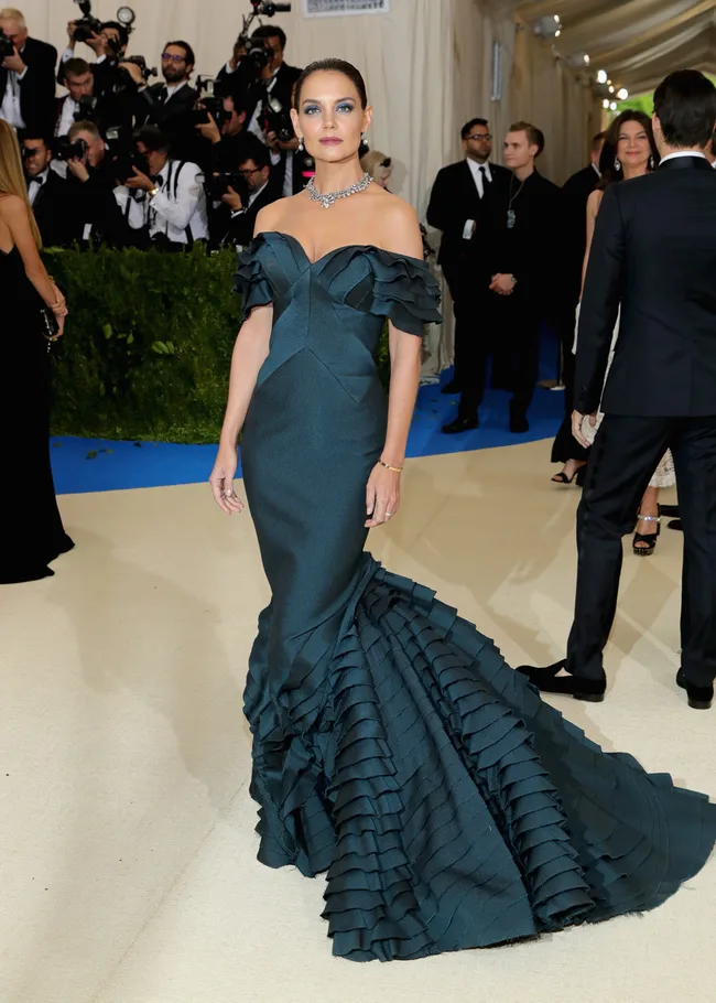 A woman in a dark teal off-shoulder gown at a formal event, with photographers in the background.