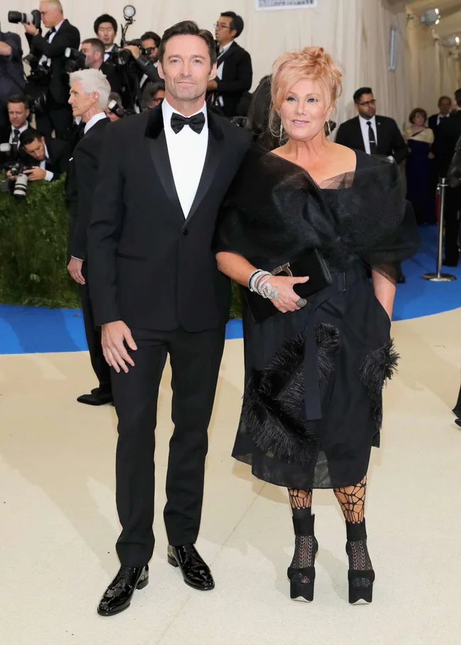 Two people in formal attire pose on a red carpet with photographers in the background.