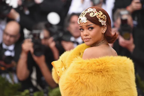 A person in a yellow fur outfit with a decorative headpiece poses for photographers at a glamorous event.