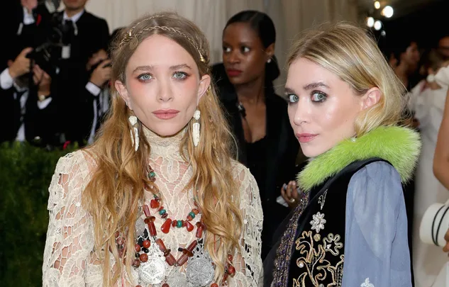 Two women in fashionable outfits at an event, wearing statement jewelry and embroidered clothing.