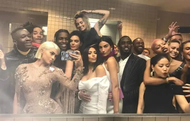 A group of well-dressed people taking a selfie in a bathroom with a tiled wall and mirror.