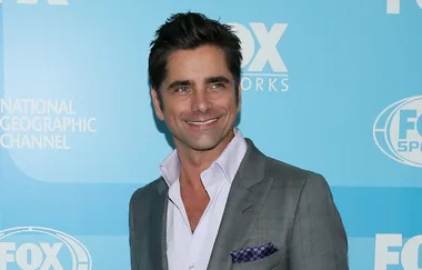 A person in a grey suit with a light blue background featuring FOX logos and text.