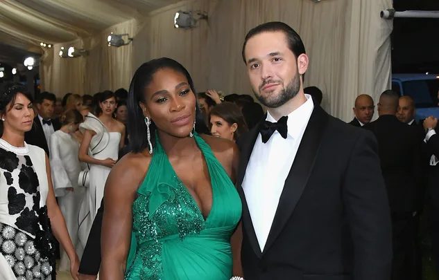 A couple dressed elegantly at a formal event, the woman in a green gown, the man in a tuxedo, surrounded by other guests.