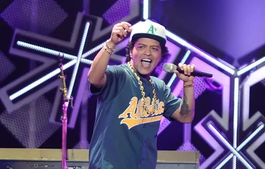 Singer performing energetically on stage, wearing an Athletics jersey and cap, holding a microphone.