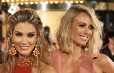 Two women smiling at an event, wearing elegant earrings and sparkly dresses.