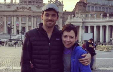 A couple posing in front of St. Peter's Basilica in Vatican City, with arms around each other and smiling.