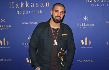 A person poses in front of a blue backdrop at Hakkasan Nightclub event, wearing a dark jacket and necklace.
