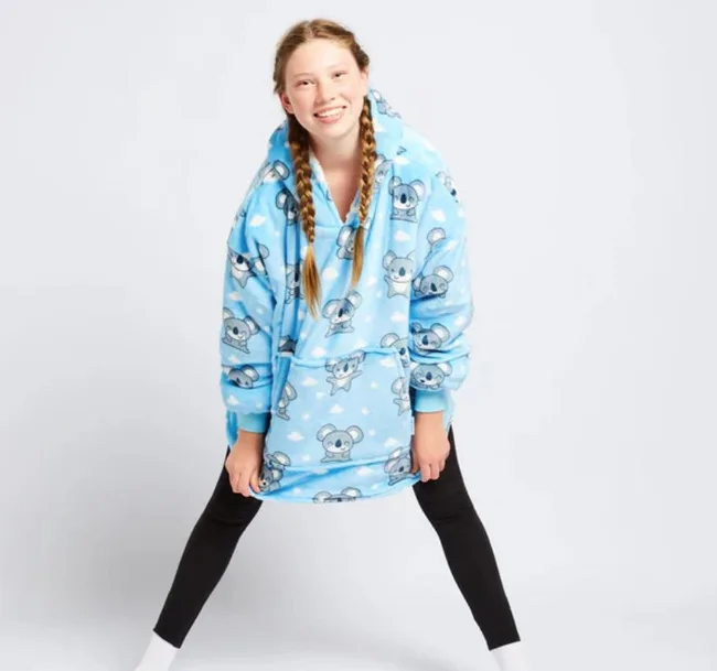 Girl in blue koala-patterned oversized hoodie, smiling, with braided hair, wearing black leggings and white socks.