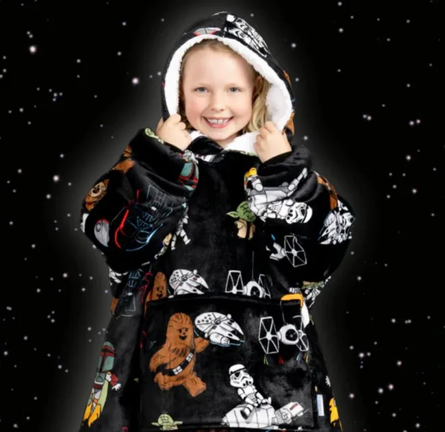 Child smiling while wearing a Star Wars-themed hoodie with characters and ships on a starry background.