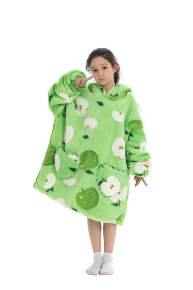 A child in a green apple-patterned oversized hoodie poses playfully against a white background.