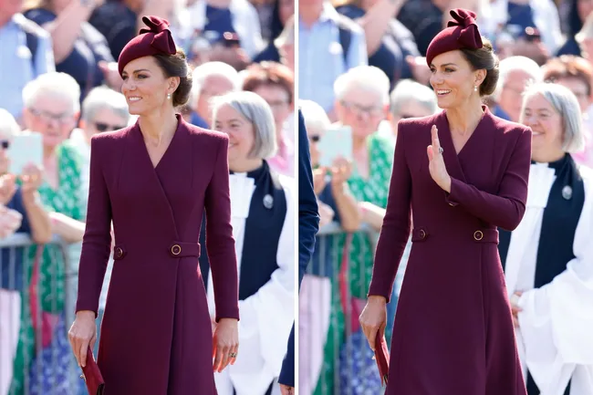 Kate Middleton in a burgundy coat dress and hat, smiling and waving to the crowd.