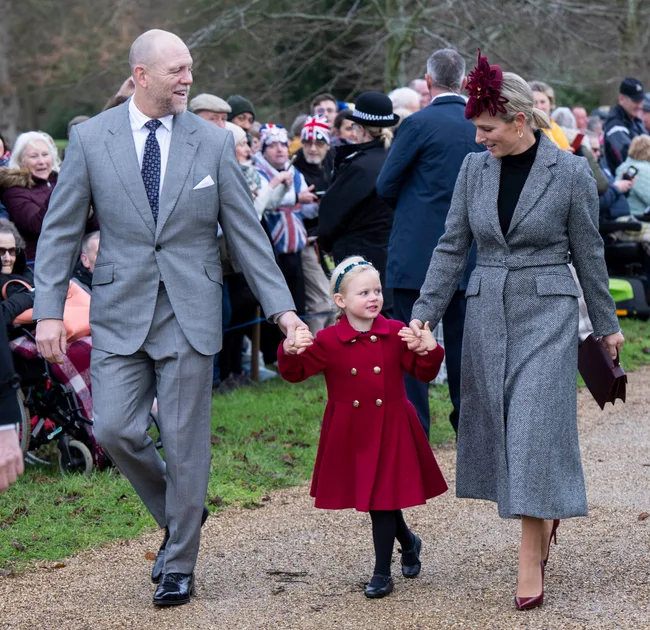 A family dressed in formal attire walks hand in hand, surrounded by a crowd with Union Jack flags.