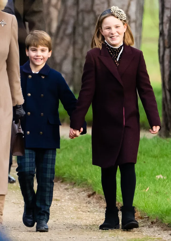 Two children walking together, holding hands, outdoors in winter coats, smiling.