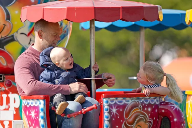 Father with baby and young girl on a colorful amusement park teacup ride, baby smiling and girl leaning over.