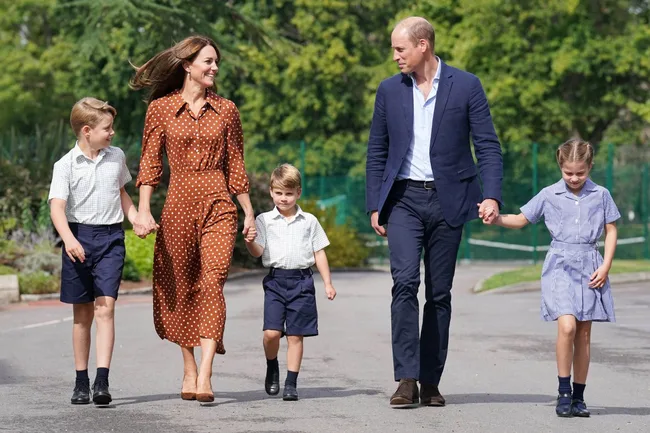 Family walking together outdoors, holding hands, dressed in casual smart attire on a sunny day.