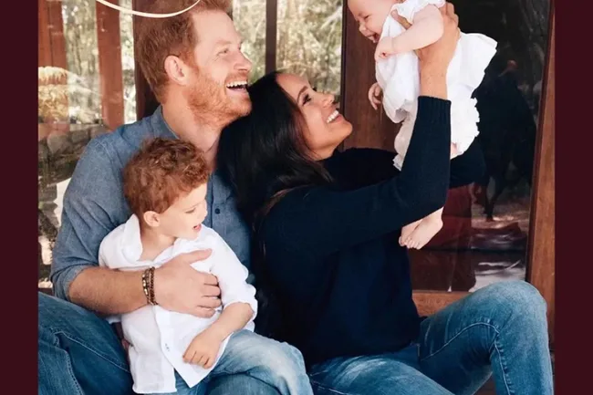 A family smiles and interacts warmly on a porch, with a baby held up playfully in the air.