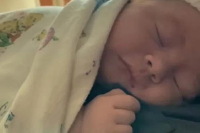 A newborn baby wrapped in a blanket, peacefully sleeping.