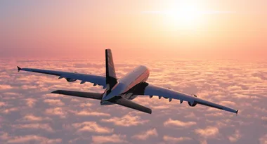 Airplane flying above clouds at sunset with a vibrant orange sky.