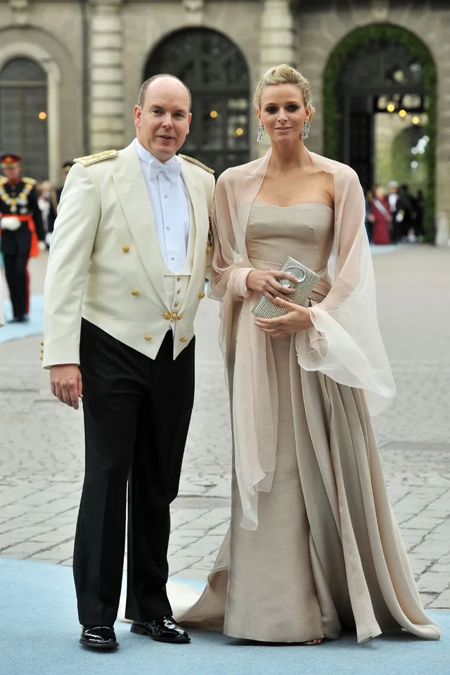 Elegant couple in formal attire at an outdoor event, with the woman in a strapless gown and holding a clutch.