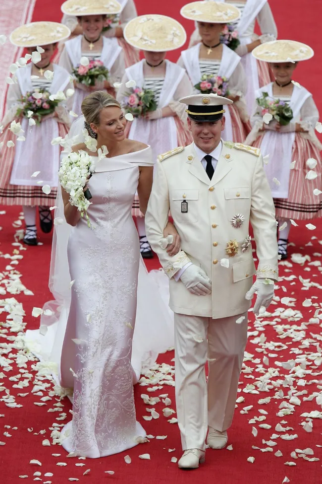 Royal wedding scene: Bride in an elegant white gown with groom in uniform, surrounded by flower girls in traditional attire.