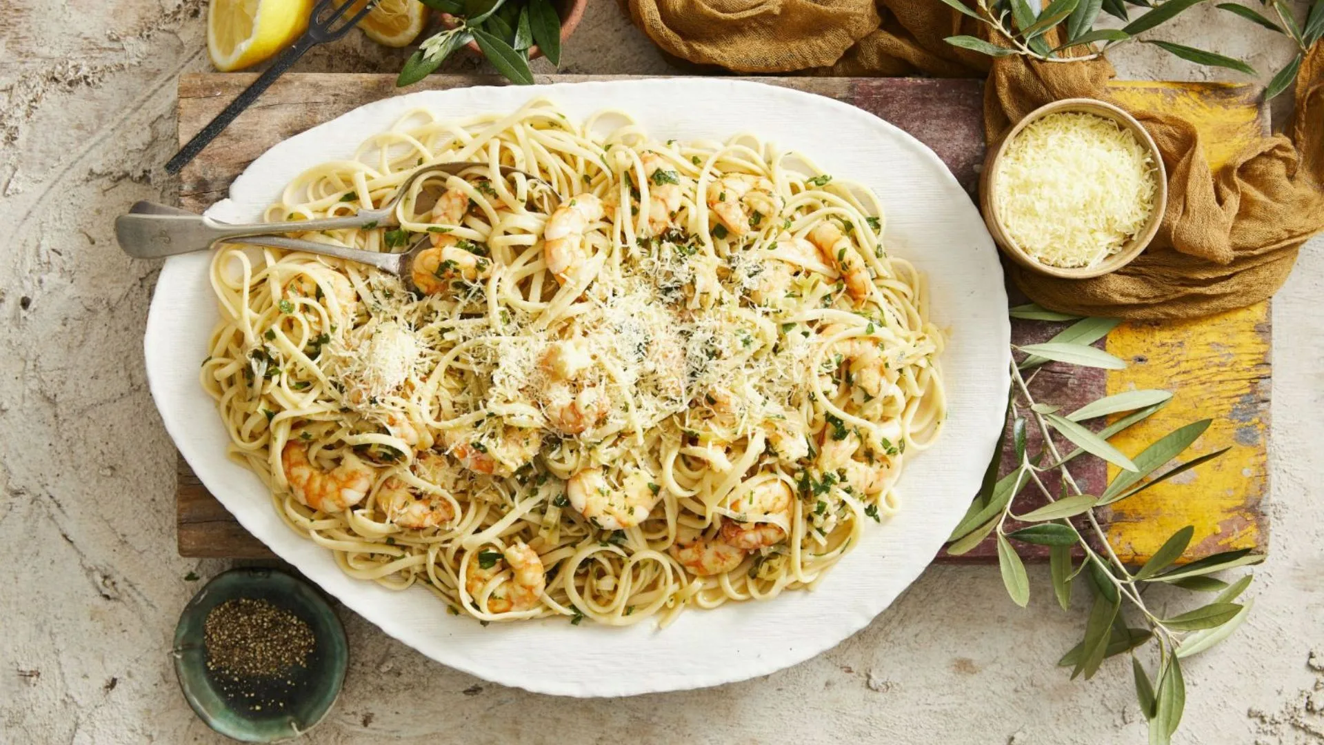Plate of prawn linguine garnished with parmesan, served with lemon wedges and herbs.
