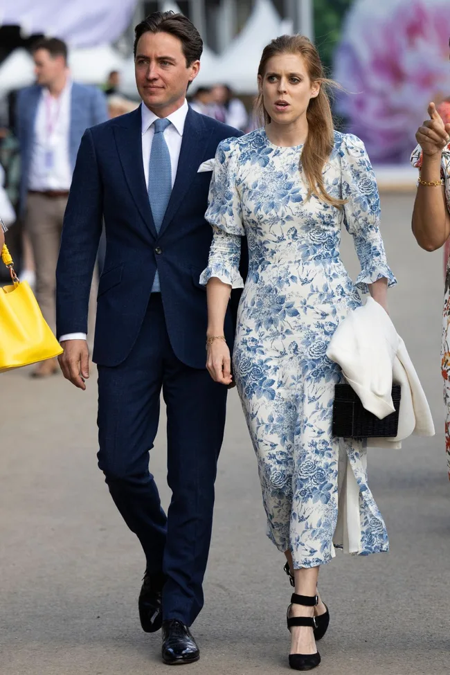 Man in blue suit and woman in blue floral dress walking together, outdoors.