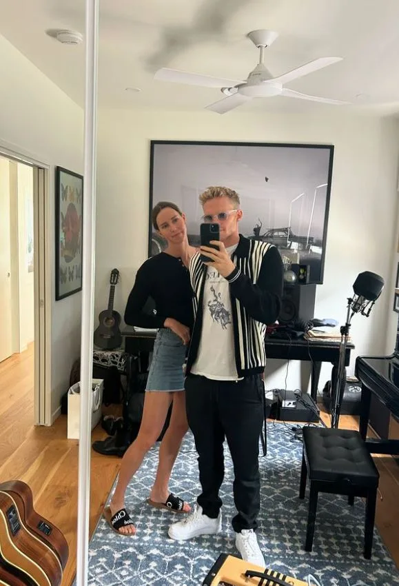 A couple takes a selfie in a music-themed room with guitars and a microphone visible.