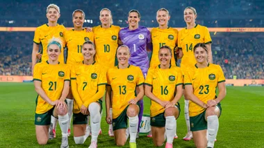 Australian women's national soccer team, the Matildas, posing on the field in yellow jerseys.