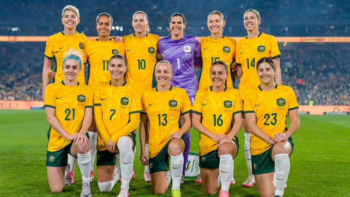 Australian women's national soccer team, the Matildas, posing on the field in yellow jerseys.