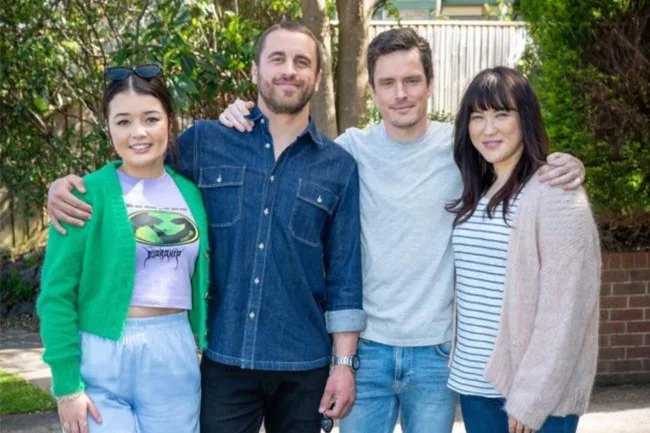 Group photo of four people outdoors, smiling and posing with arms around each other.
