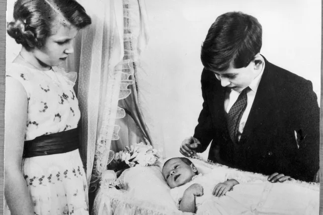princess anne and king charles stare down at the cot with prince andrew