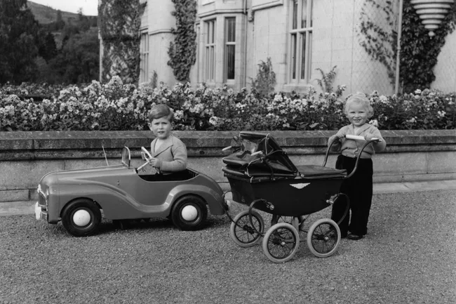 king charles plays in a fake car while princess anne pushes a pram