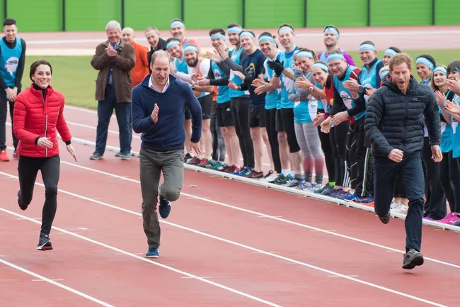 Three people running on a track with a cheering crowd in the background.