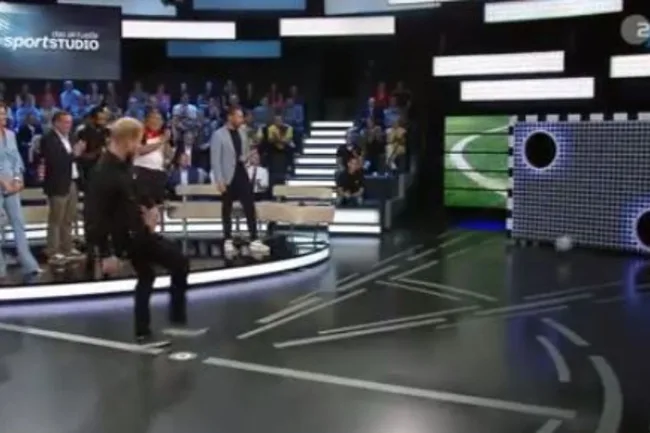 Public figure participates in a football kicking game on a TV show set with an audience.