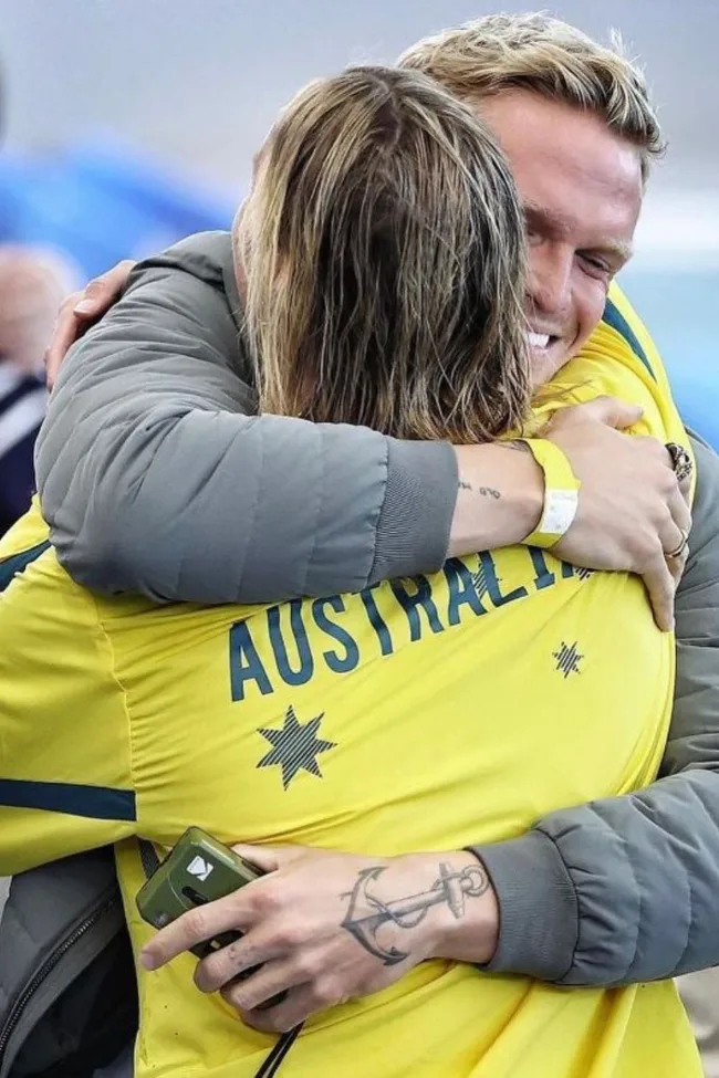 Two people embracing, one in a yellow Australian jacket with a visible tattoo.