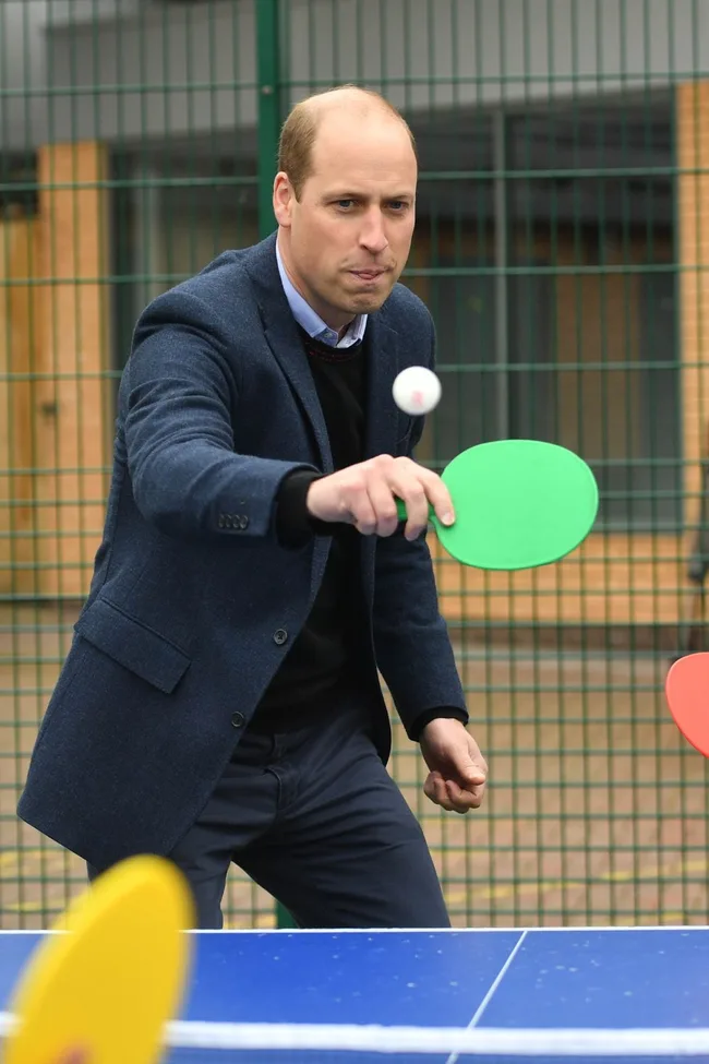 Royal family member playing table tennis with a concentrated expression, holding a green paddle.