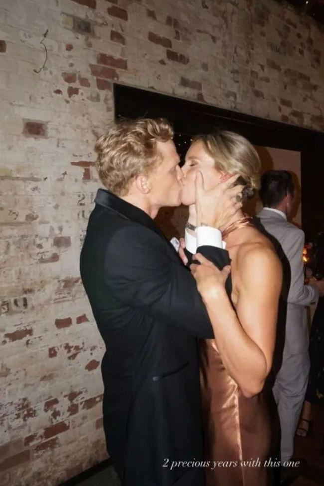 A couple kissing at an event, with a brick wall background and the text "2 precious years with this one."
