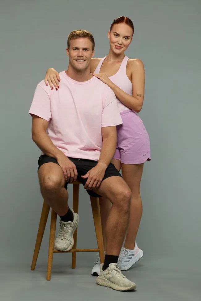 Two people in coordinated light pink athletic outfits, one seated on a stool and the other standing behind, posing for a photo.
