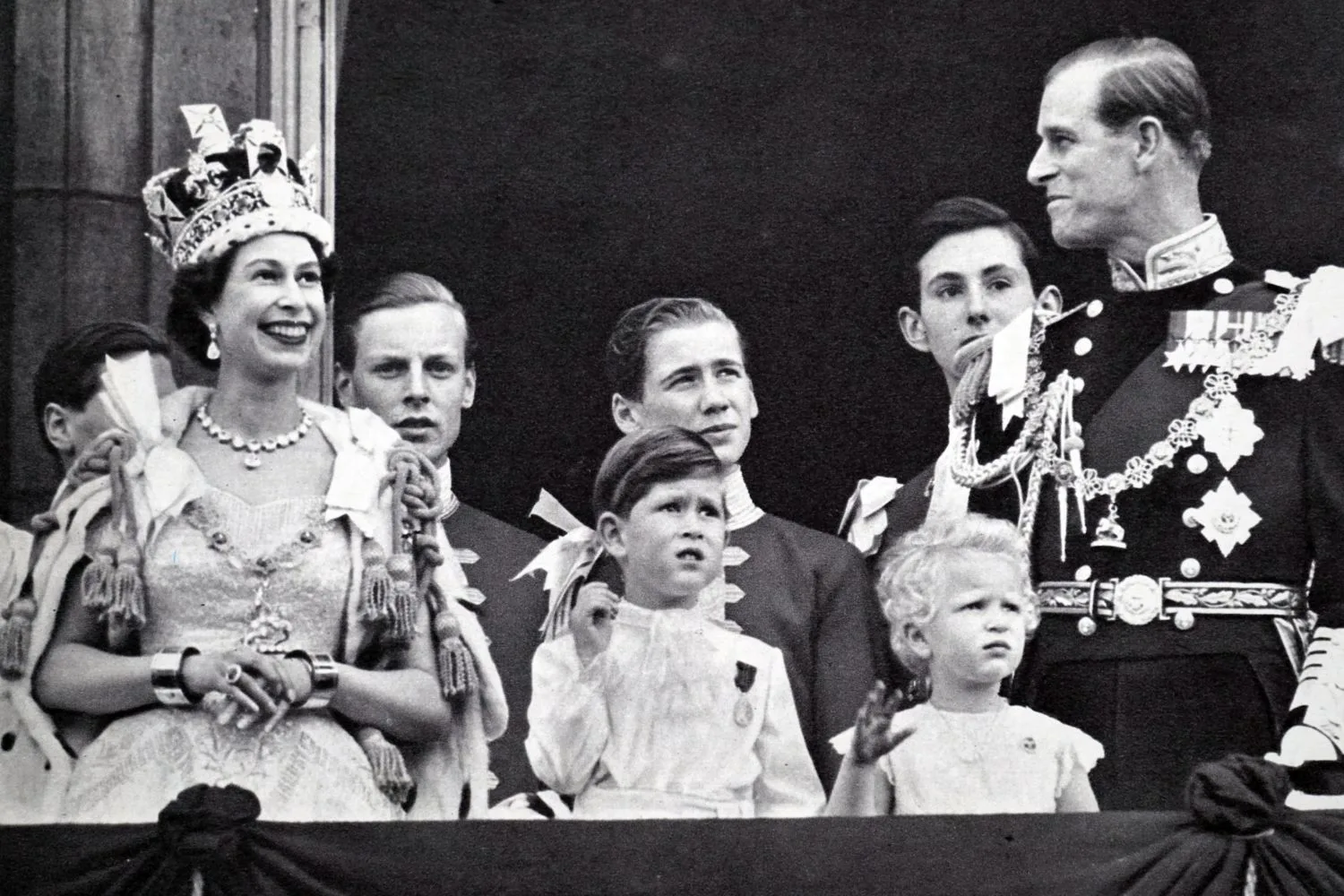 queen elizabeth coronation day. the queen and the duke exchange smiles while prince charles and princess anne look at the plane above them
