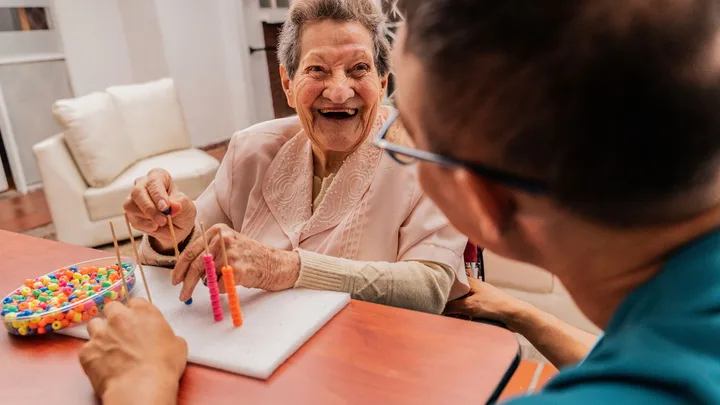 Elderly woman smiling while doing bead activity with a caregiver.