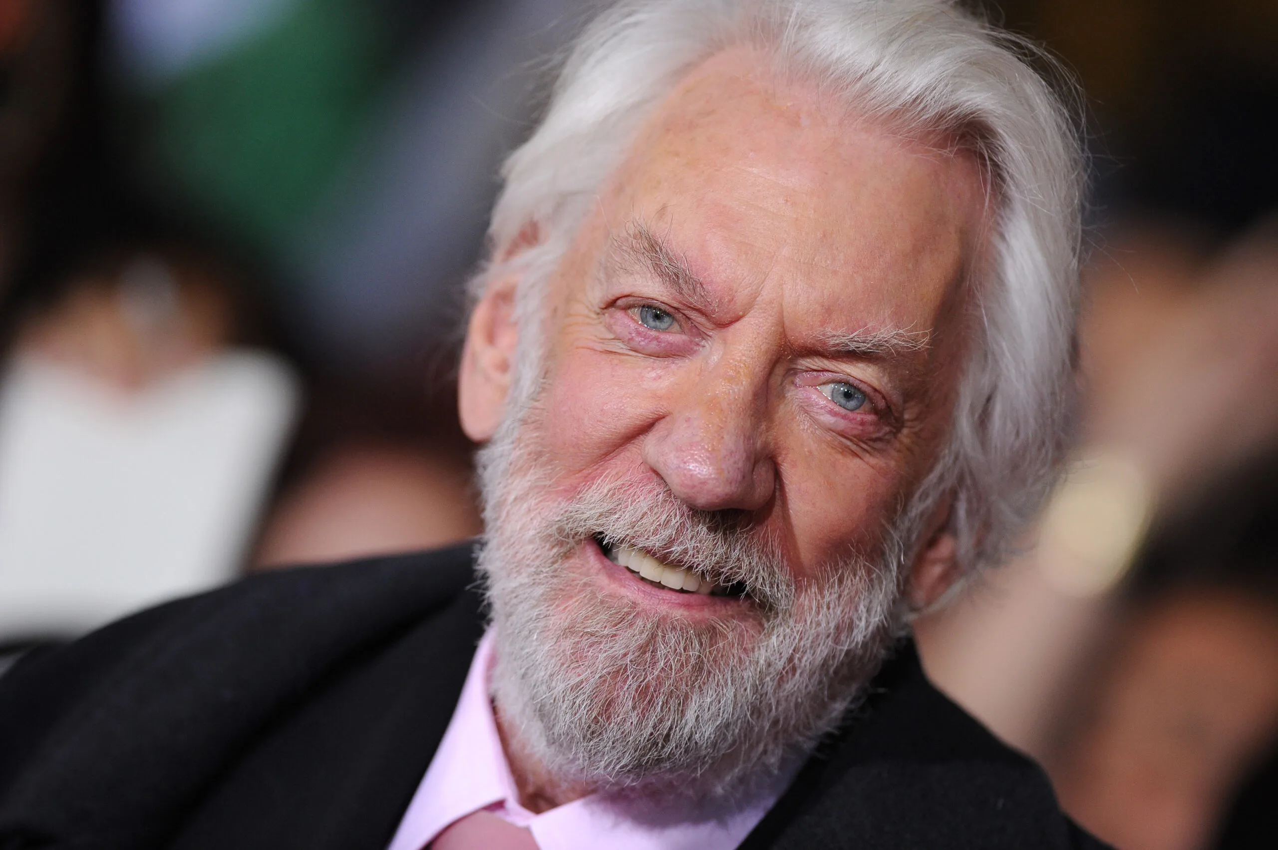 donald sutherland at a red carpet event, wearing a black suit jacket and pink shirt and tie