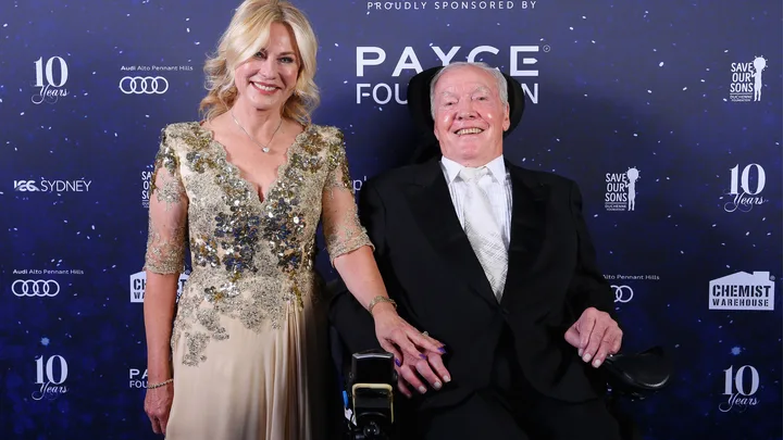 Two smiling individuals in formal attire on a dark blue starry backdrop at a charity event.