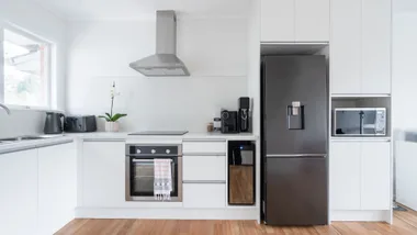 Modern kitchen with white cabinets, black appliances, a stainless steel fridge, oven, and a window on the left.