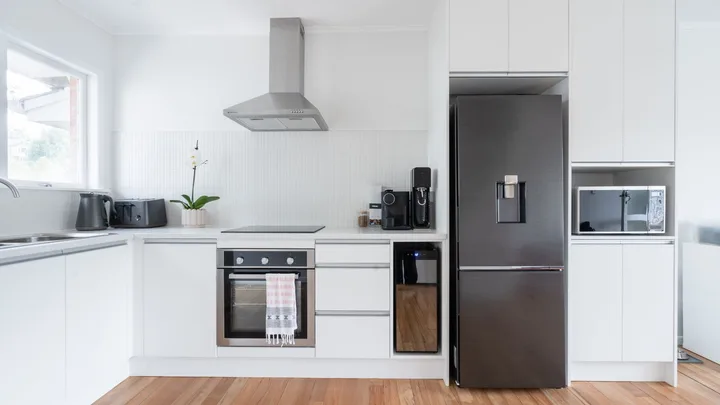 Modern kitchen with white cabinets, black appliances, a stainless steel fridge, oven, and a window on the left.